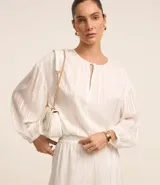 Blusa blanca de chiffon con cuello redondo y abertura en forma de gota en el frente. Tiene mangas 3/4 y rayas de hilo teñido metalizado.