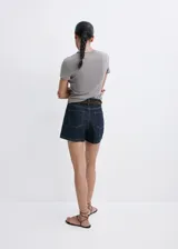 Short de denim azul oscuro con diseño de cinco bolsillos, tiro medio y cierre frontal de cremallera y botón.
