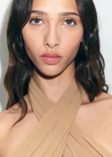 Vestido largo de gasa color tostado, con diseño recto y cuello halter cruzado con detalle drapeado. Presenta un diseño semitransparente con forro interior y cierre de cremallera en la parte posterior.