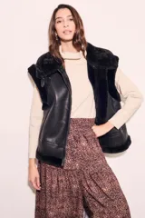 Chaleco negro de cuero sintético con cuello de piel sintética y cierre frontal con cremallera.