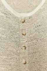 Top tipo chaleco de tejido de punto con algodón, color beige con detalles texturizados. Presenta cuello redondo, sin mangas y cierre frontal con una hilera de botones.