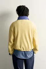 Sudadera polar de corte regular color amarillo, con cuello subido en tono azul, cierre frontal de cremallera verde y bolsillos con ribete verde. Incluye un parche gráfico de Fruit of the Loom en el pecho.