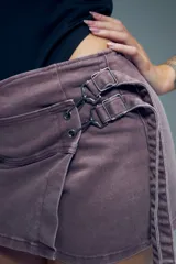 Short pollera de algodón en color negro, con diseño de falda cruzada y detalle de hebillas metálicas en la cintura. Cuenta con cierre posterior.