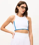 Top deportivo femenino confeccionado en microfibra, de color blanco con vivos en azul, escote redondo, copa y breteles anchos.