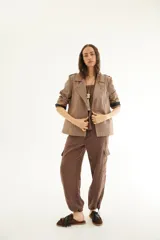 Chaqueta corta de inspiración motoquera color beige, confeccionada en lino fantasía, sin forro, con cierres decorativos, broches de presión y bolsillos delanteros funcionales. Presenta detalle bajo el cuello y en vueltas de mangas en color mostaza y rayas.