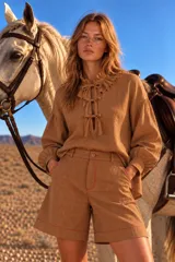 Blusa blanca de manga larga con cuello alto y volados, cierre frontal con lazos y diseño holgado.