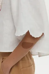Camisa crop blanca de lino con silueta relajada, cuello clásico y mangas cortas. Presenta bordados de tigres en el frente y detalles ornamentales en los hombros.