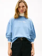 Buzo de felpa celeste Tommy Hilfiger con cuello redondo, manga larga y puños de canalé. Cuenta con el logotipo de la marca bordado en tipografía script en el pecho y detalles de botones dorados decorativos en el hombro.