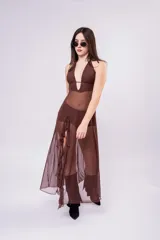 Vestido largo de tul color marrón con diseño de top halter y falda con volados laterales. Presenta una estructura de malla semitransparente que aporta movimiento y elegancia.