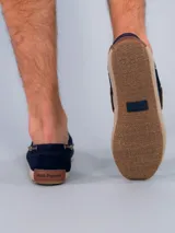 Mocasines estilo náutico de gamuza azul marino con cordones de cuero marrón. Presentan una suela con detalle de yute trenzado alrededor del borde y base de goma.