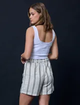 Short color crema con finas rayas verticales grises, pretina elastizada con cordón de ajuste, bolsillos delanteros y traseros.