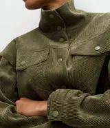 Campera Marfinno de pana verde militar, con cuello alto, cierre frontal con botones a presión, bolsillos con solapa en el pecho y cordón ajustable en el bajo.