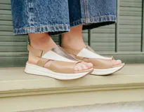 Sandalias de cuero combinadas en tonos tostado, nude y detalles metalizados dorados, con diseño de tiras cruzadas y textura efecto reptil en la parte superior. Cuentan con suela de plataforma baja y tira ajustable en el talón.