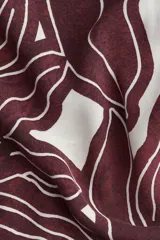 Vestido midi con cuello camisero, botonadura frontal y mangas cortas. Presenta un estampado abstracto en tonos marrón oscuro y blanco, elástico en la cintura y cinturón para atar.