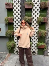 Buzo tipo hoodie color crudo, de calce oversize, con cuello alto y estampa pequeña de una carita sonriente azul en el pecho.
