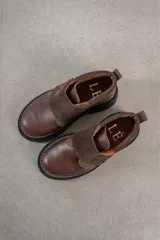 Botinetas de caña baja con suela track gruesa, combinando cuero negro en la puntera, gamuza marrón en el lateral y detalles de textura animal print tipo serpiente en tonos marrones. Presenta un cierre de solapa con velcro en el empeine.