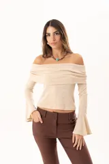 Blusa beige con hombros descubiertos, confeccionada en tela elástica con destellos de lurex. Presenta mangas largas con terminación acampanada y diseño ajustado al cuerpo.