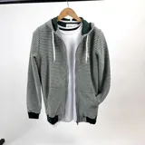 Campera con capucha, confeccionada en algodón rústico a rayas horizontales verdes y crudas, con cierre frontal y bolsillos laterales. Tiene puños y cintura en color verde oscuro.