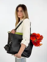 Cartera tote de cuero genuino color negro, con costuras visibles a contratono, asas dobles para hombro, parche frontal con logo grabado y charms colgantes en forma de estrella y mini monedero.