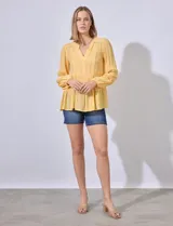 Blusa blanca de gasa con escote en V y apliques de puntilla en el frente. Manga larga con puño elastizado.