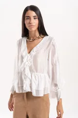 Blusa de tejido liviano color blanco, con escote en V y volados frontales. Presenta mangas largas amplias con puños fruncidos y un volado en el ruedo que le otorga un calce fluido y cómodo.