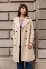 Trench clásico de largo midi en color beige, con diseño de doble abotonadura, solapas amplias, detalles en hombros y correas ajustables en los puños.