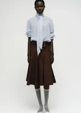 Blusa de textura ligera en color celeste, con cuello alto envolvente y detalle de fular integrado. Presenta mangas largas con puños abotonados y un diseño de corte recto.