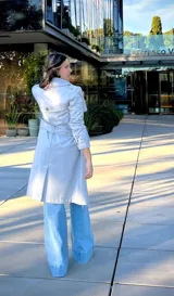 Trench coat gris de corte clásico con doble botonadura, solapas amplias, cinturón ajustable con hebilla y mangas con trabillas en los puños.
