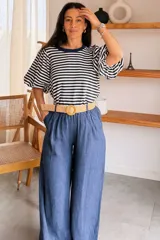 Pantalón palazzo de corte ancho, color azul jean, con pinzas frontales, bolsillos laterales y presillas en la cintura. Incluye un cinturón tejido de rafia con hebilla circular revestida.