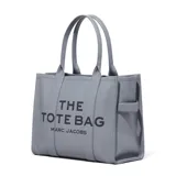 Cartera tipo tote de cuero granulado en color gris, con diseño estructurado y asas superiores. Presenta el logo estampado en el frente con la inscripción The Tote Bag Marc Jacobs.