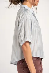 Camisa oversize celeste y beige con rayas verticales, cuello camisero, mangas cortas y cierre frontal con botones.
