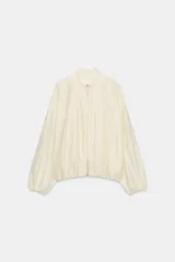 Chaqueta bomber de cuello subido y manga larga, con acabado satinado en color beige. Presenta pliegues frontales, bolsillos laterales ocultos en costura y cierres elásticos en puños y cintura. Cierre frontal con cremallera.