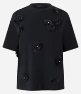 Remera Cortelle de algodón en color negro, con cuello redondo y mangas cortas. Presenta un diseño de corte holgado decorado con aplicaciones florales tridimensionales en relieve con detalles brillantes en el centro.