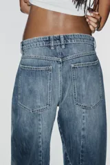 Jeans de tiro medio y corte barrel con diseño de perneras curvadas, tiro medio, trabillas para cinturón y cinco bolsillos. Presenta lavado clásico y costuras pespunteadas decorativas en la parte delantera.