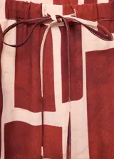 Pantalón fluido de tiro medio con estampado geométrico en tonos bordó y beige, cintura elástica con cordón ajustable, bolsillos laterales y diseño de pernera recta.