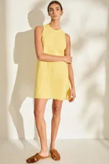 Vestido corto de lino italiano, sin mangas y con cuello redondo a la base. Presenta detalles desflecados en el cuello y costura central vertical.