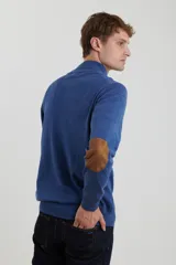 Sweater de punto gris con medio cierre frontal, cuello alto y coderas en tono marrón. Presenta un diseño clásico con puños y ruedo acanalados.