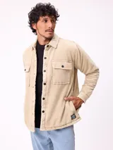 Sobrecamisa de pana color beige, con cierre frontal de botones a presión, dos bolsillos frontales con solapa y bolsillos laterales. Presenta cuello clásico y diseño acolchado con forro interior.