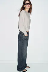 Chaqueta de punto color beige claro, de cuello redondo y manga larga abullonada con puño ajustado. Cierre frontal cruzado con botones plateados.