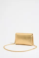 Bolso bandolera de piel color dorado, tamaño mini, con solapa y cierre magnético. Tiene asa de cadena y bolsillo interior. El exterior está personalizado con un logo metálico.