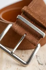 Cinto marrón de gamuza con hebilla metálica plateada.