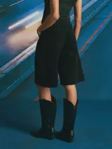 Bermuda de corte amplio y tiro alto, confeccionada en tejido de pana color negro. Presenta diseño de cinco bolsillos, cierre frontal con botón y bragueta, y largo por encima de la rodilla.