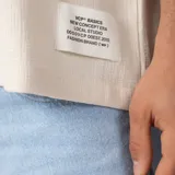 Remera oversize de lino entramado color blanco off-white, con cuello redondo, mangas cortas de hombro caído y etiqueta aplicada en el borde inferior.