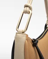 Bolso de hombro tricolor en forma de media luna, confeccionado en material sintético con textura granulada. Cuenta con un compartimento principal con cierre de cremallera, tirador con nudo negro, bolsillo interior con cremallera, asa corta tubular en tono claro con detalle metálico y logo grabado en la parte frontal.