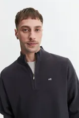 Buzo de tejido de punto texturizado color gris oscuro o carbón, con cuello alto y cierre frontal parcial plateado. Presenta un pequeño logo bordado en blanco en el pecho.