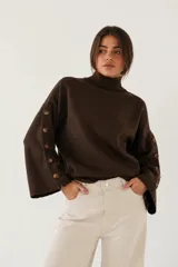 Sweater de bremer color chocolate con cuello alto y mangas largas con detalle de botones en los puños. Presenta un diseño holgado con aberturas laterales en el ruedo.