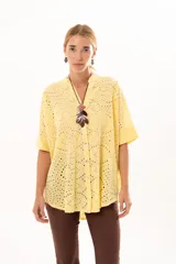 Camisa de corte oversize confeccionada en tela bordada con diseño calado, color amarillo. Presenta cuello mao, cierre frontal con botones y mangas cortas amplias.