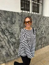Conjunto compuesto por remera de manga larga oversize a rayas horizontales blancas y negras con escote bote, y pantalón negro de corte flared.