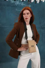 Phonebag pequeña color mostaza, confeccionada en cuero sintético, con solapa frontal y correa ajustable con logo de la marca.