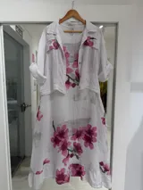 Set de vestido midi y casaca de lino color blanco, con estampado de flores de cerezo en tonos rosados y ramas grises. El vestido es sin mangas de corte acampanado, y la casaca es de manga 3/4 con bolsillos frontales con solapa.